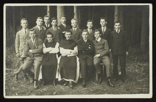 Gruppenaufnahme von vierzehn jungen Männern und Geistlichen im Wald