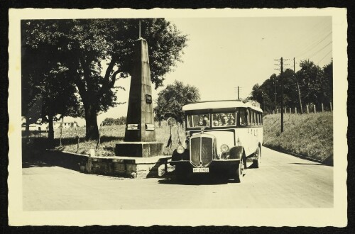 Omnibus vor einem Wegweiser-Obelisken an der Straße nach Lindau und Kempten