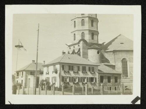 Festlich geschmücktes Gebäude und Kirchturm mit Maibaum